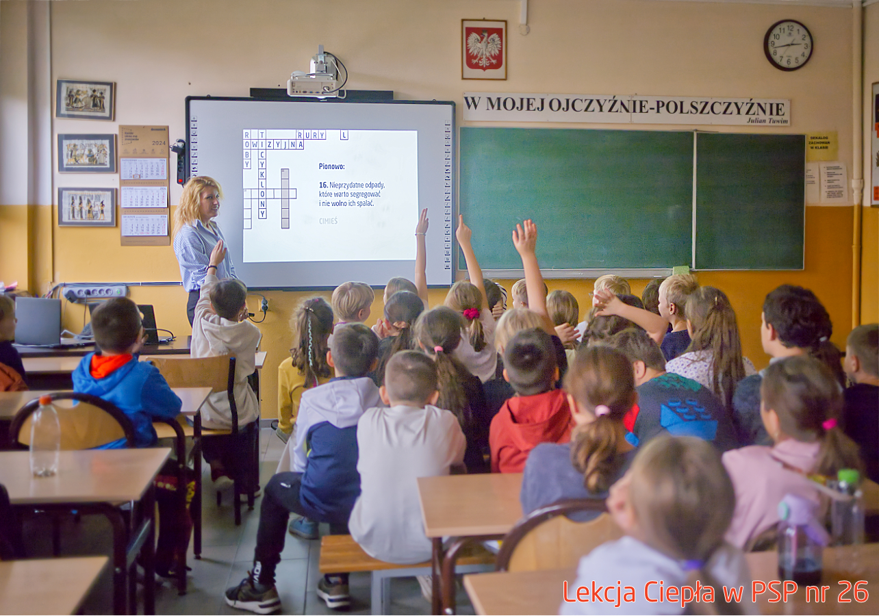 Pracownik „RADPEC” S.A. prowadzi lekcję ciepła dla uczniów klasy IV PSP nr 26. Stoi przed grupą uczniów. W tle znajduje się ekran z jednym ze slajdów prezentacji.