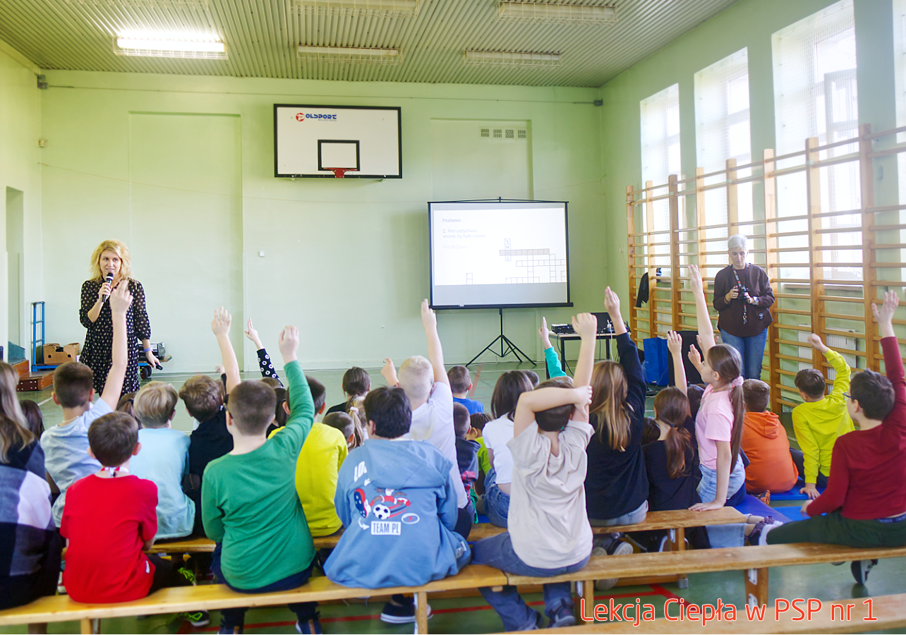 Pracownik „RADPEC” S.A. prowadzi lekcję ciepła dla uczniów klasy IV PSP nr 1. Stoi przed grupą uczniów. W tle znajduje się ekran z jednym ze slajdów prezentacji.