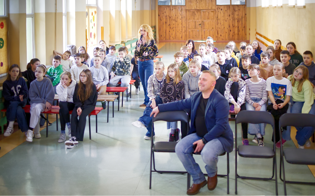 Pracownik RADPEC-u stoi z mikrofonem wśród uczniów w trakcie podsumowania III edycji kampanii proekologicznej pn. „Lekcje ciepła” w Publicznej Szkole Podstawowej nr 3 w Radomiu.
