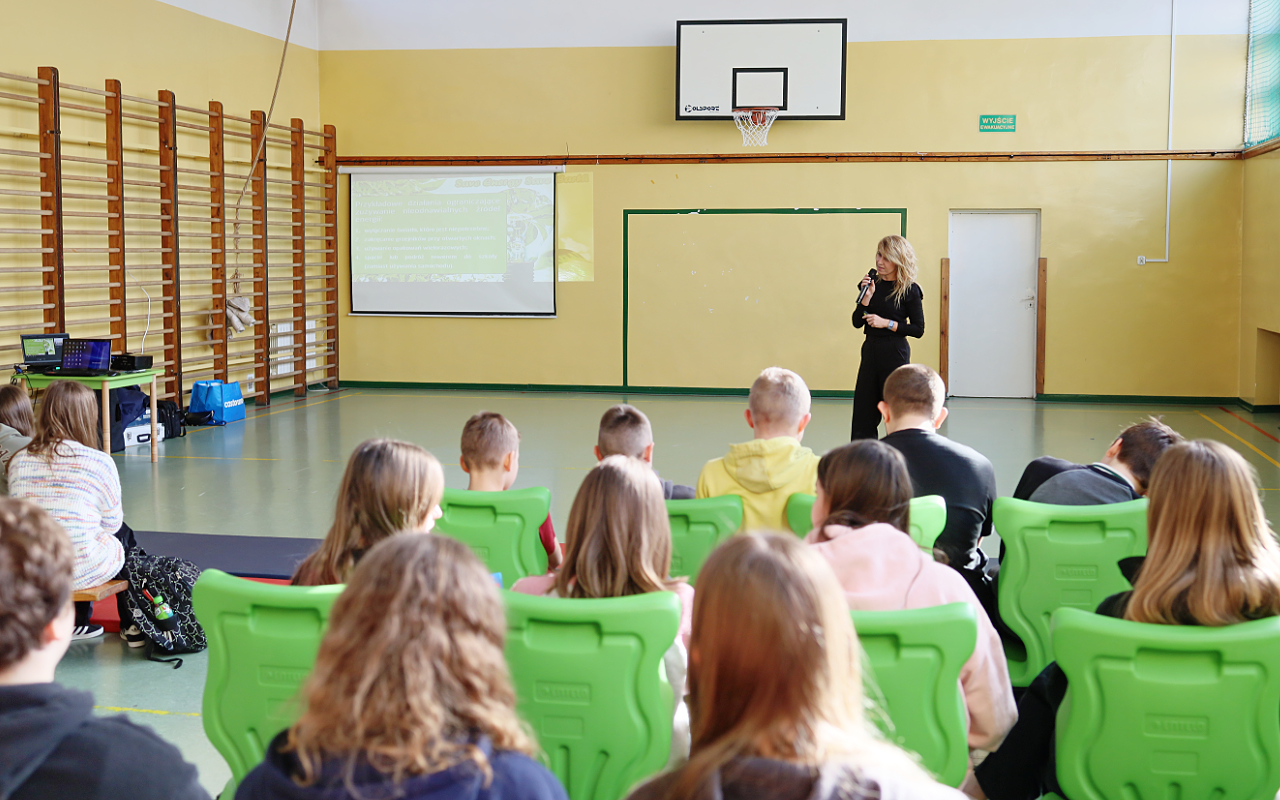 Pracownik „RADPEC” S.A. prowadzi lekcję ciepła dla uczniów klasy VI jednej z radomskich szkół. Stoi przed grupą uczniów. W tle znajduje się ekran z jednym ze slajdów prezentacji.